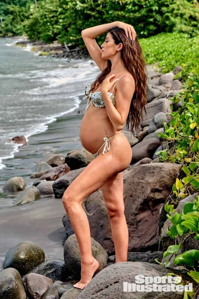 Nicole Williams English poses on the rocks edging the beach in a sparkly teal bikini set.